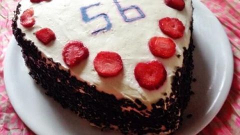 Eine herzförmige Erdbeersahnetorte steht auf einem weißen Teller, dekoriert mit Erdbeerscheiben und der Zahl 56.