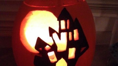Ein leuchtender Halloween-Kürbis mit schwarzen Flächen, der eine gespenstische Szene hinter einem Vollmond darstellt.