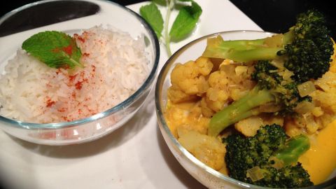 Blumenkohl und Brokkoli in Kokos-Curry-Soße liegen in einer Schüssel, daneben dampfender Reis, verziert mit Minze.