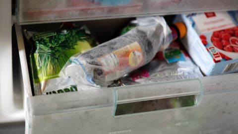 Eine Getränkeflasche liegt in einem Gefrierfach, um schnell zu kühlen, umgeben von gefrorenem Gemüse und Obst.