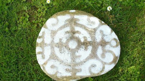 Eine verzierte Beton Gehwegplatte liegt auf grünem Gras, geschmückt mit einem eleganten Muster in Weiß.