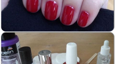 Rote, perfekt lackierte Fingernägel liegen auf einem Untergrund mit Nagellackfläschchen und Zubehör zur Maniküre.