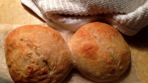 Zwei frisch gebackene Bäckerbrötchen liegen nebeneinander auf einer Arbeitsfläche, umgeben von einem Küchentuch.