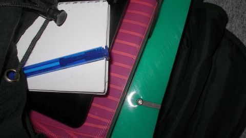 Ein grüner Aktentasche liegt offen und enthält einen Notizblock und einen blauen Stift, bereit für das Falten von Hemden oder Blusen.