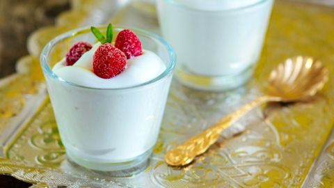 Zwei transparente Gläser mit frischem Joghurt und Himbeeren stehen auf einem eleganten Tablett aus Silber.