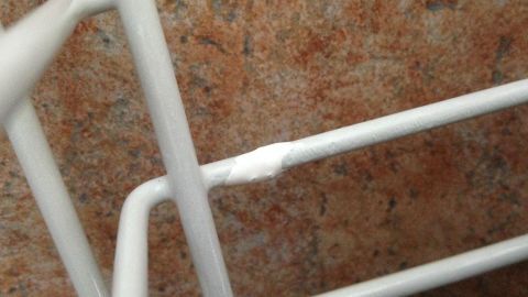 Ein weißer Besteckkorb, der eine beschädigte Stelle zeigt, steht auf einer braunen, strukturierten Oberfläche.