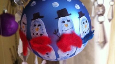 Eine farbenfrohe Weihnachtskugel zeigt fröhliche Schneemänner mit roten Schals in einer festlichen Umgebung.