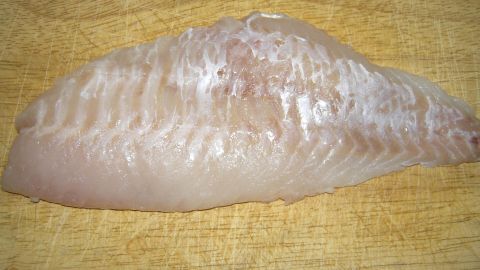 Ein frisches Fischfilet liegt auf einem Holzbrett, bereit zum schnellen Entgräten in einer Küchenumgebung.