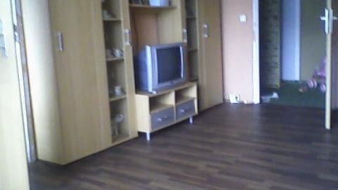 Ein Wohnzimmer mit Laminatboden, Holzschränken und einem Röhrenfernseher auf einem kleinen Schrank; gemütliches Ambiente.