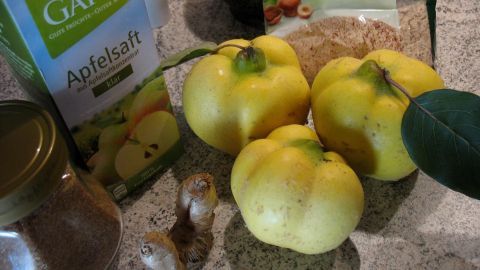 Gelbe Quitten liegen auf der Arbeitsfläche, umgeben von Apfelsaft und Zutaten für die Quitten-Quark-Torte mit Streuseln.