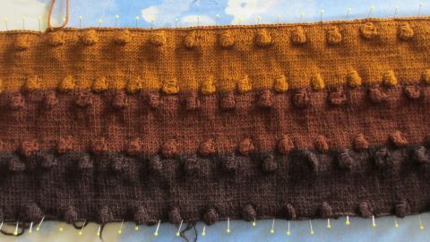 Eine gestrickte Textiloberfläche mit verschiedenen Braun- und Orangetönen rollt sich nicht mehr ein und liegt flach.