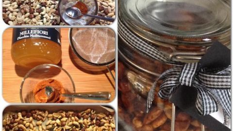 Geröstete Nüsse sind in einem Glas mit einem karierten Band. Neben dem Glas sind Gewürze wie Chili und Honig zum Verfeinern sichtbar.