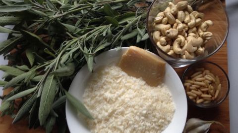 Frische Salbeiblätter liegen neben einer Schüssel mit Cashews und geriebenem Parmesan, alles bereit für Pesto.