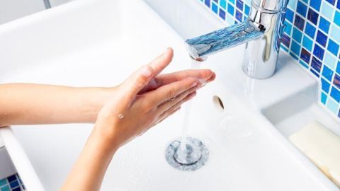 Hände werden im Waschbecken mit klarem Wasser gewaschen, während farbige Fliesen die Wand dahinter verzieren.