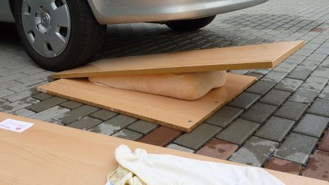 Ein Tempur Kopfkissen liegt auf einer Holzplatte zwischen zwei anderen Platten, während ein Auto darüber steht und es trocknet.