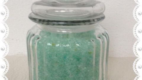 Ein Glasbehälter mit mintgrünem Fußpeeling steht auf einer Oberfläche, bereit zur Anwendung an den Füßen.