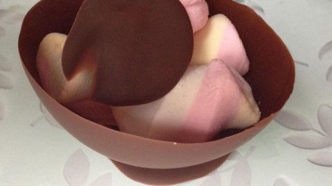 Eine Schokoschale hält bunte Desserts, während sie auf einem eleganten Teller serviert wird.