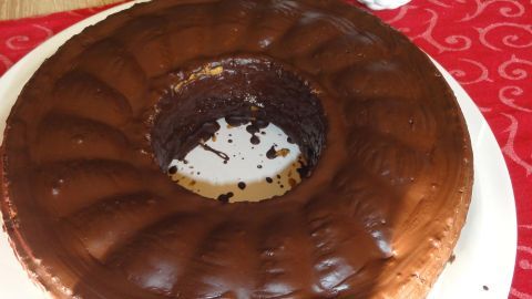 Ein mit Schokolade glasierter Gewürzkuchen steht auf einem weißen Teller auf einem roten Tischläufer neben zwei weißen Vasen.