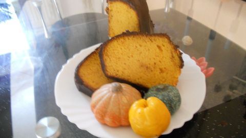 Scheiben von Kürbiskuchen auf einem weißen Teller, verziert mit kleinen Zierkürbissen, auf einem Glastisch platziert.