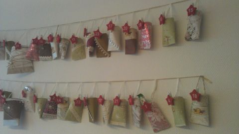 Papierrollen sind aufgehängt, nummeriert als Adventskalender, an einer Wand mit dekorativen Rotsternen von 1 bis 24.