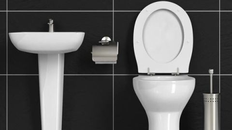 Toilette steht offen neben Waschbecken und Papierspender in einem Bad mit schwarzen Fliesenwänden.