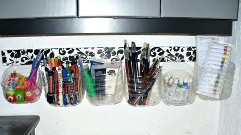 Ablagebehälter aus Saftcontainern hängen an der Wand, gefüllt mit Stiften und Bürobedarf in einem kreativen Arbeitsbereich.