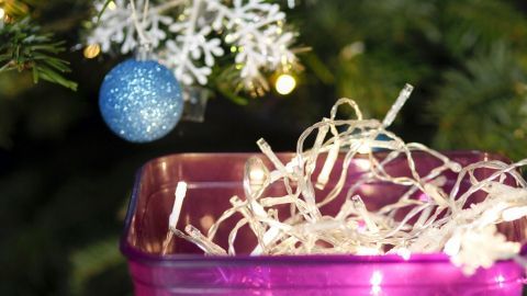 Ein künstlerisch dekorierter Behälter bewahrt Lichterketten auf, während ein Weihnachtsbaum im Hintergrund schimmert.