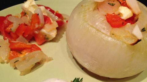 Gefüllte Gemüsezwiebel mit Schafskäse steht auf einem grünen Teller, umgeben von buntem Gemüse und einer Joghurtsoße.