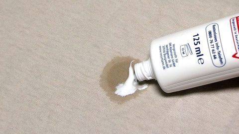 Eine Zahnpasta wird auf einen Obstfleck auf einem hellen Stoff aufgetragen, um den Fleck zu entfernen.