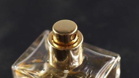 Ein Parfumflakon mit goldenem Sprühkopf steht vor einem dunklen Hintergrund und verströmt wohlriechenden Raumduft.