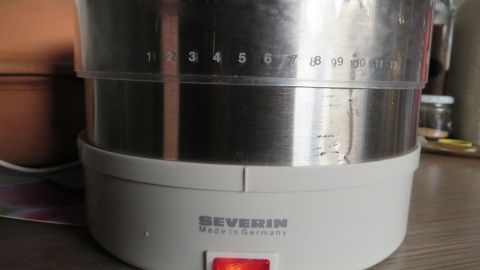 Ein silberner Tortenring steht auf einem Tisch, während er genutzt wird, um einen Kuchen in einer gemütlichen Küche zu formen.