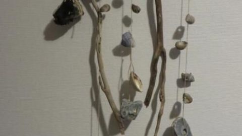 Ein hölzerner Mobile hängt an einer Wand und zeigt verschiedene Muscheln und Steine, die kunstvoll angeordnet sind.
