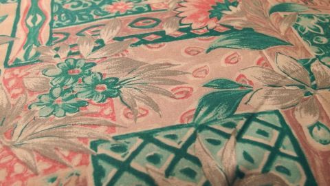 Ein bunter Stoff mit floralem Muster liegt flach auf einer Oberfläche und zeigt verschiedene grüne und rosafarbene Designs.