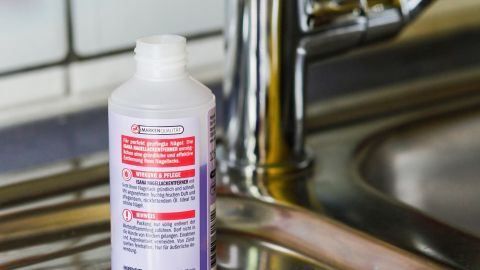 Eine Flasche Reinigungsmittel steht neben einem Wattepad auf einer Spüle, bereit zum Armaturen reinigen in der Küche.