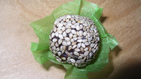 Ein Pralinenförmchen umhüllt eine Sesamkugel, die auf einer Holzoberfläche präsentiert wird.