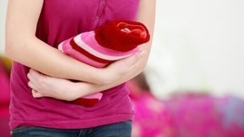 Eine Person hält ein gefaltetes rotes und pinkes Handtuch, während sie in einem Raum mit verschwommenem bunten Hintergrund steht.