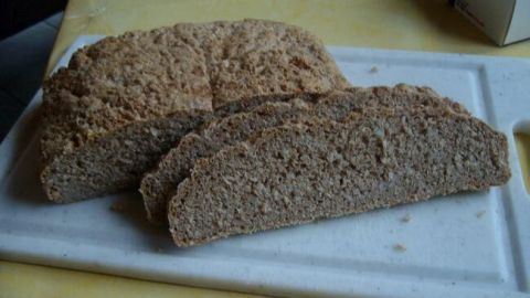 Dinkel-Schrot-Brot liegt auf einem Schneidebrett, frisch geschnitten, umgeben von einer hellen, einfachen Küche.