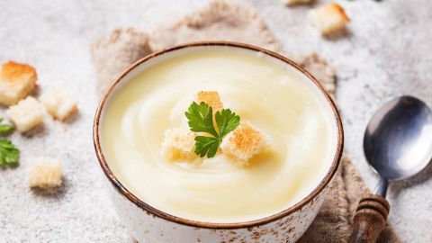 Eine Schüssel mit cremiger veganer Kartoffelsuppe, garniert mit Croutons und einem Blatt Petersilie, auf einem rustikalen Untergrund.