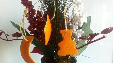 Bunte Christbaum-Aufhänger hängen dekorativ an einer Pflanze, umgeben von rotem und grünem Blattwerk im Hintergrund.