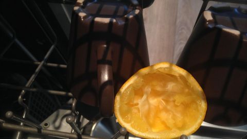 Eine halbe Orange liegt in einem Geschirrspüler neben zwei dunklen Tassen, um unangenehme Gerüche zu neutralisieren.