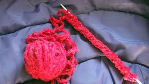 Ein rotes Strickprojekt liegt auf einem blauen Stoff, während die Nadeln mit Wolle für viele Strickmodelle vorbereitet sind.