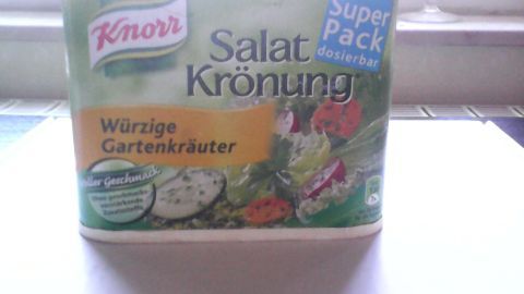 Ein Karton mit Knorr Salatkrönung steht auf einer hellen Fläche. Er enthält würzige Gartenkräuter für Salate.