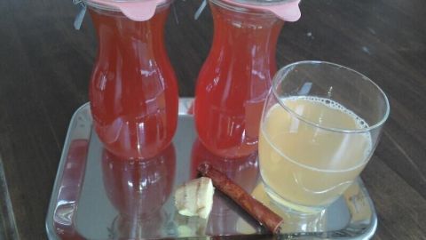 Zwei Glaskaraffen mit roten Sirup und ein Glas mit gelbem Getränk auf einem silbernen Tablett in einer gemütlichen Umgebung.
