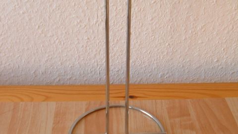 Ein Gitarrenhalter aus Metall steht auf einem Holzregal, bereit zur Wandmontage für die sichere Aufbewahrung einer Gitarre.