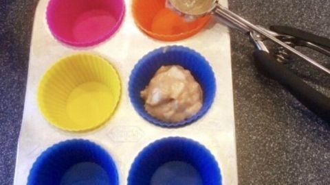 Bunte Muffinförmchen werden mit einem Eisportionierer leicht befüllt, auf einer grauen Arbeitsplatte platziert.