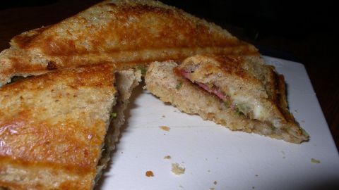 Ein knuspriges Pizza-Sandwich, aufgeschnitten, zeigt geschmolzenen Käse und Wurst, liegt auf einem Schneidebrett.