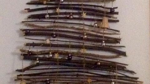 Ein Weihnachtsbaum aus Ästen hängt an einer Wand, geschmückt mit kleinen Glocken und einer Sternspitze.
