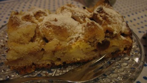 Ein Apfelkuchen mit knusprigen Butterstreuseln liegt auf einem gläsernen Teller, umgeben von festlichem Geschirr in einer gemütlichen Umgebung.