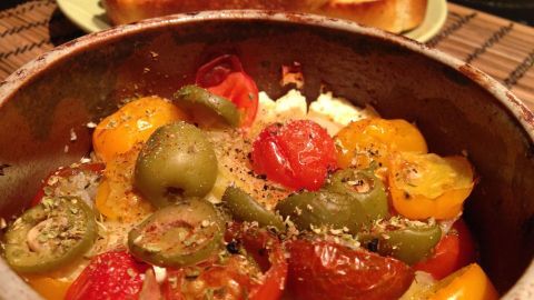 Ein bunter Schafskäse-Tomaten-Paprika-Topf mit frischen Kräutern wird in einer Schüssel serviert, umgeben von Brot.