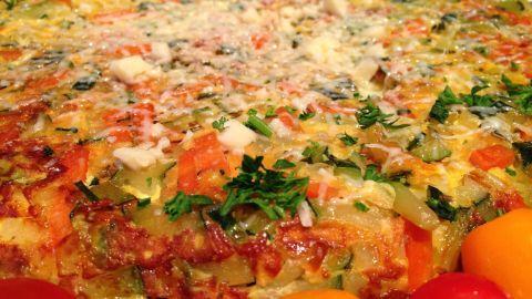 Eine bunte Frittata mit Karotten und Zucchini liegt auf einem Teller, umgeben von frischen Kirschtomaten und leichtem Parmesan.